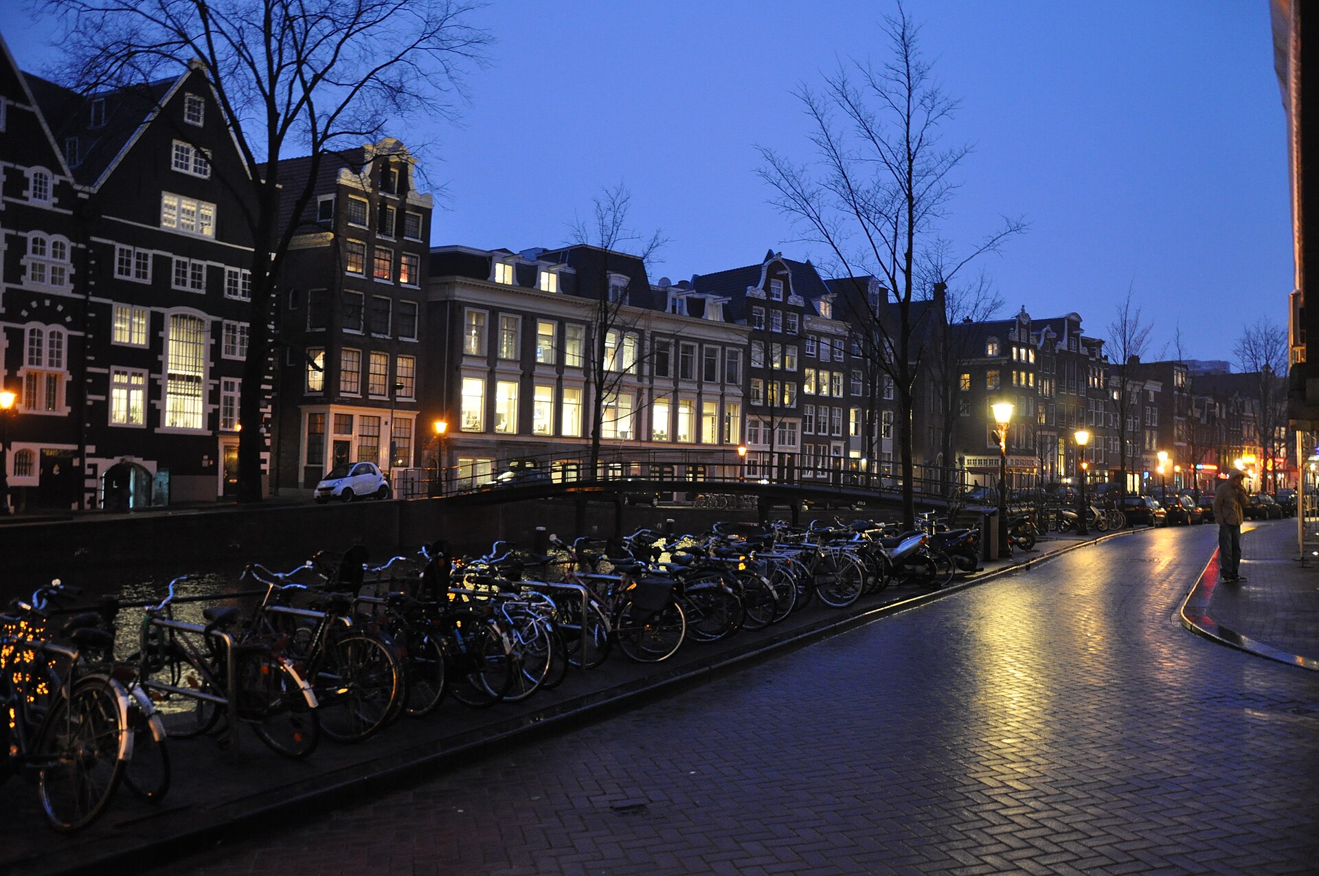 Un canal de Ámsterdam al anochecer, con casas iluminadas y bicicletas en las barandillas