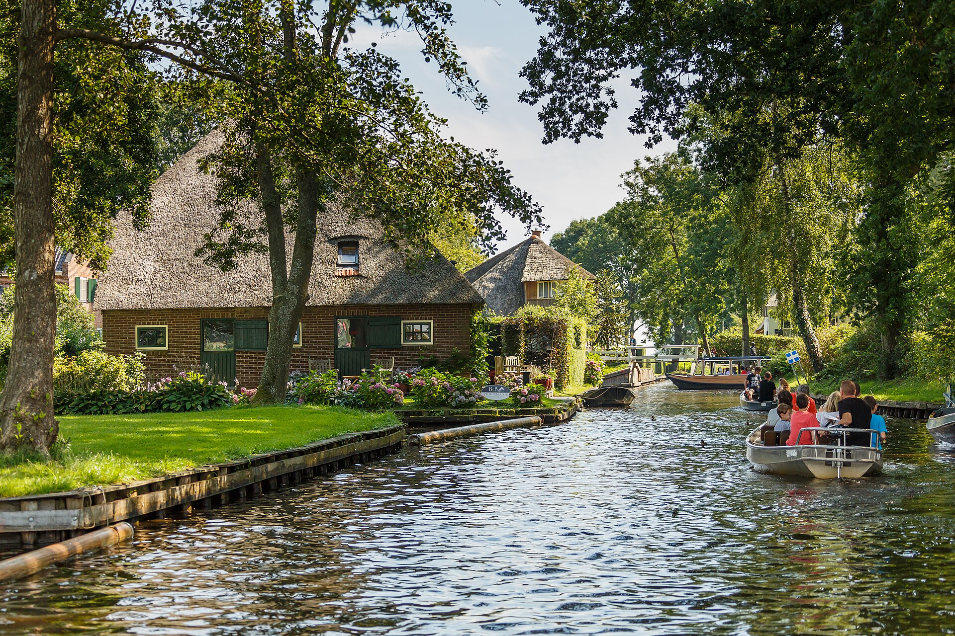 Un canal de Giethoorn con una granja de techo de paja, césped verde y pequeñas barcas