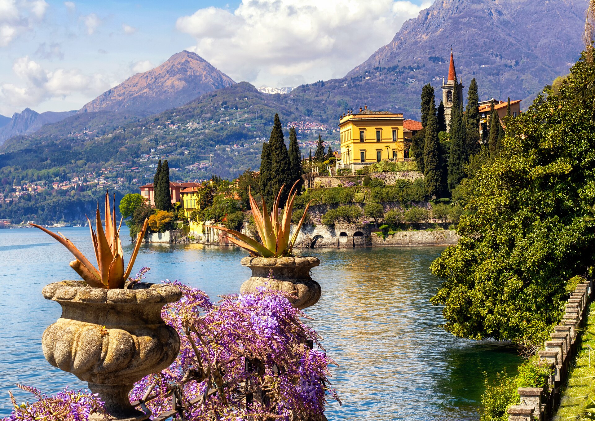Flores y jarrones en una terraza junto al lago en Varenna, con el lago de Como y montañas al fondo