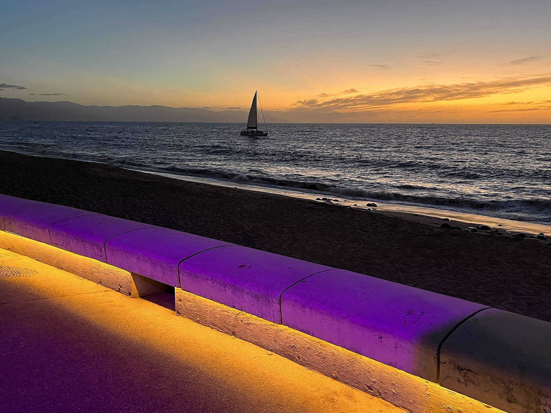 Sunset over Banderas Bay from Puerto Vallarta's seafront promenade, with a sailboat on the water